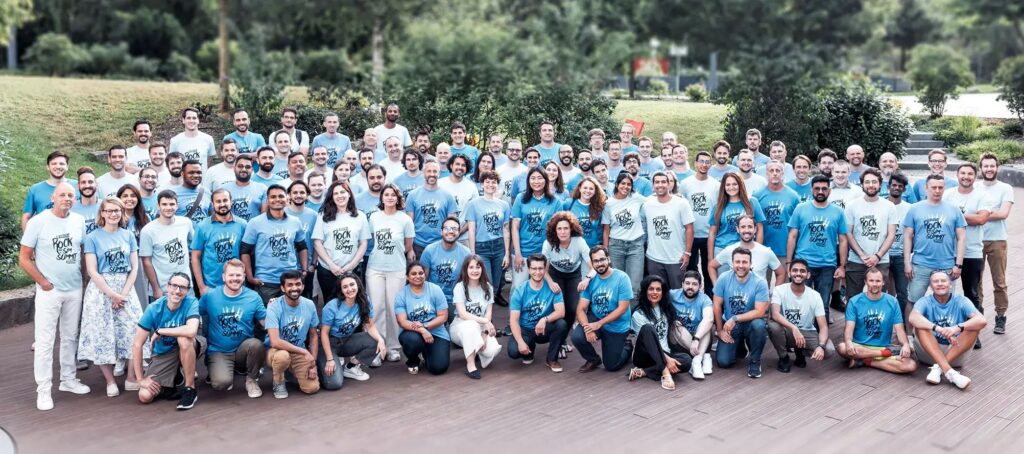 The SimScale team all wearing blue and light blue posing in front of a green area