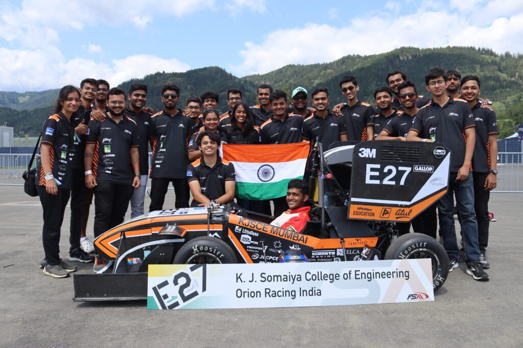 Team Orion Racing India standing behind their Formula Student car and holding the Indian flag