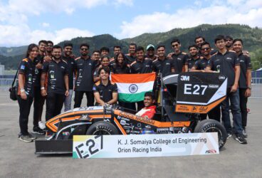 Team Orion Racing India standing behind their Formula Student car and holding the Indian flag